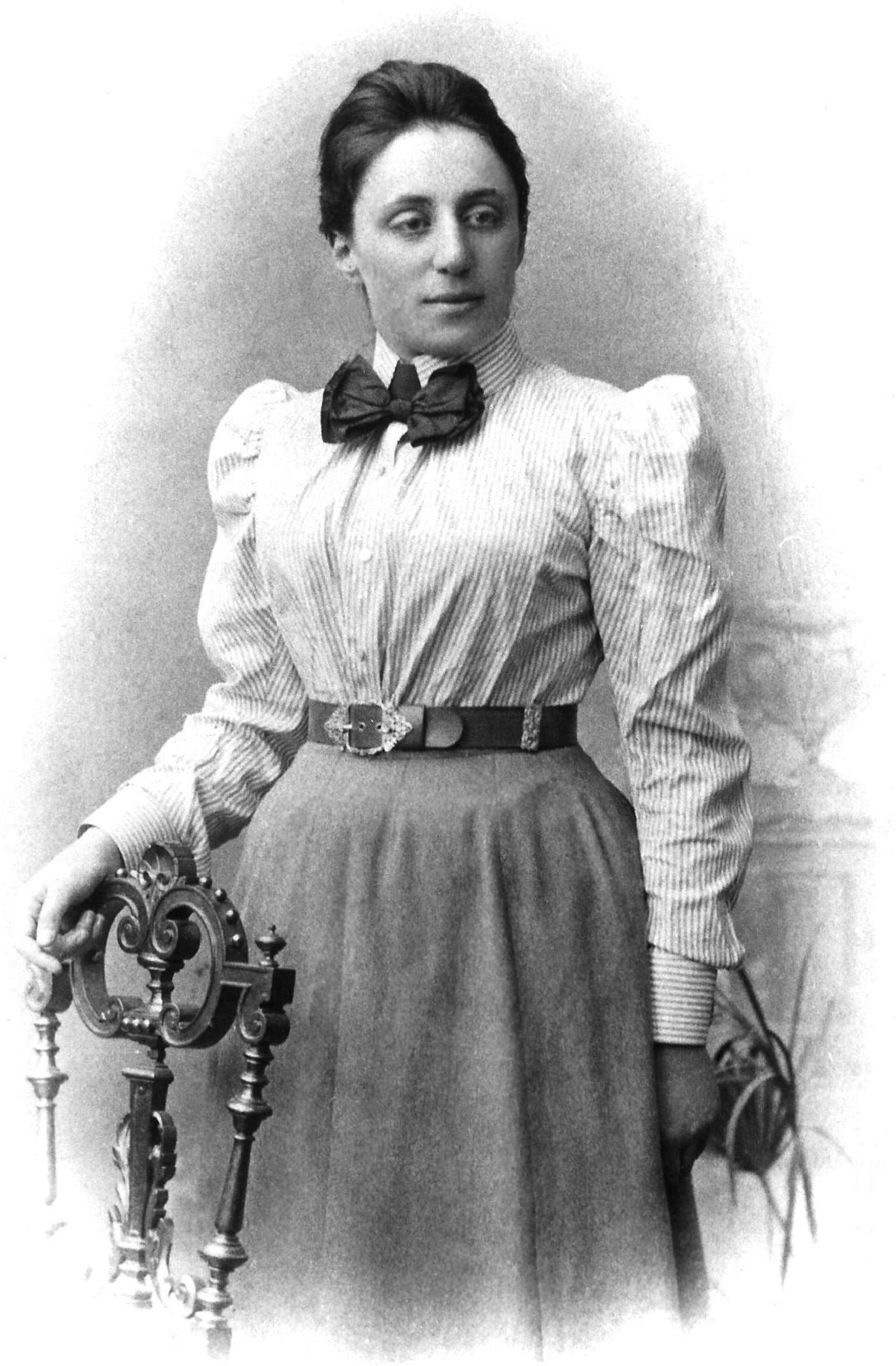 Fotografía de Emmy Noether de pie junto a una silla.